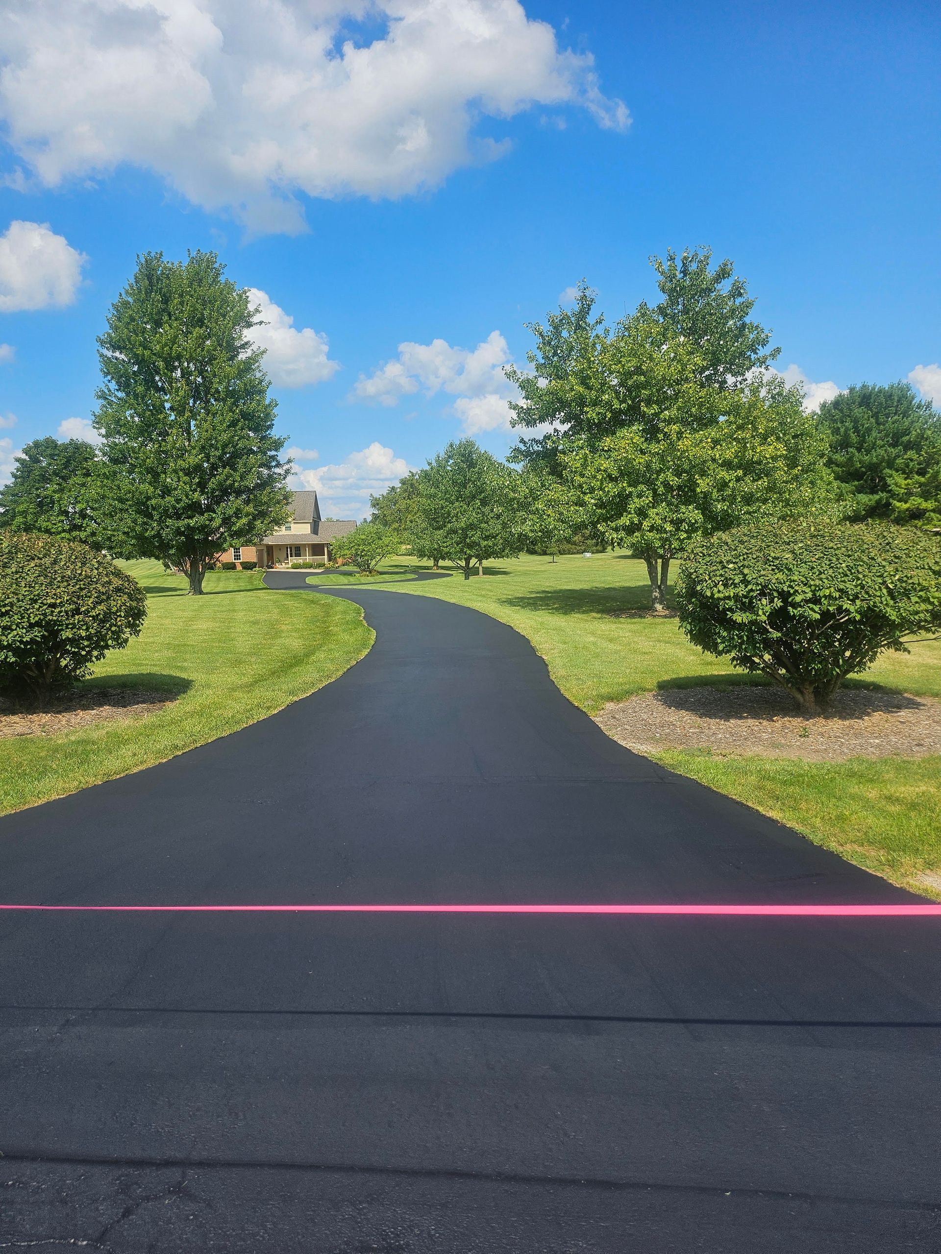 A road with trees on both sides and a house in the background