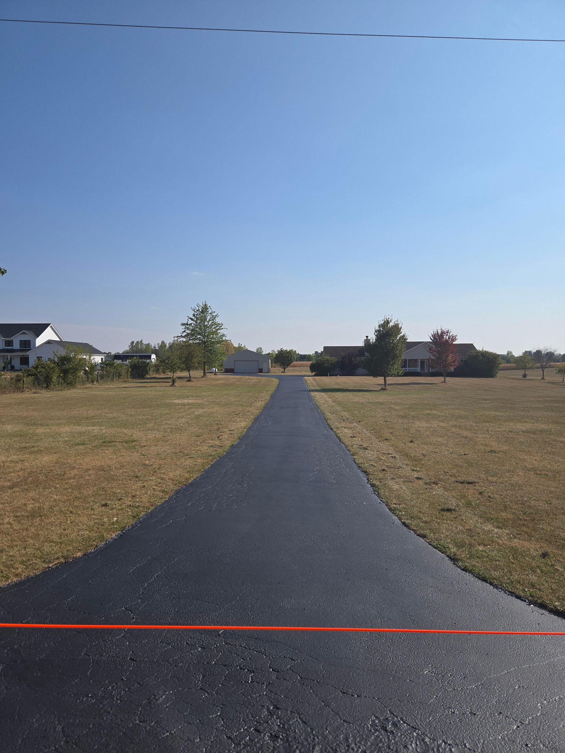 A road that is going through a field with houses in the background.