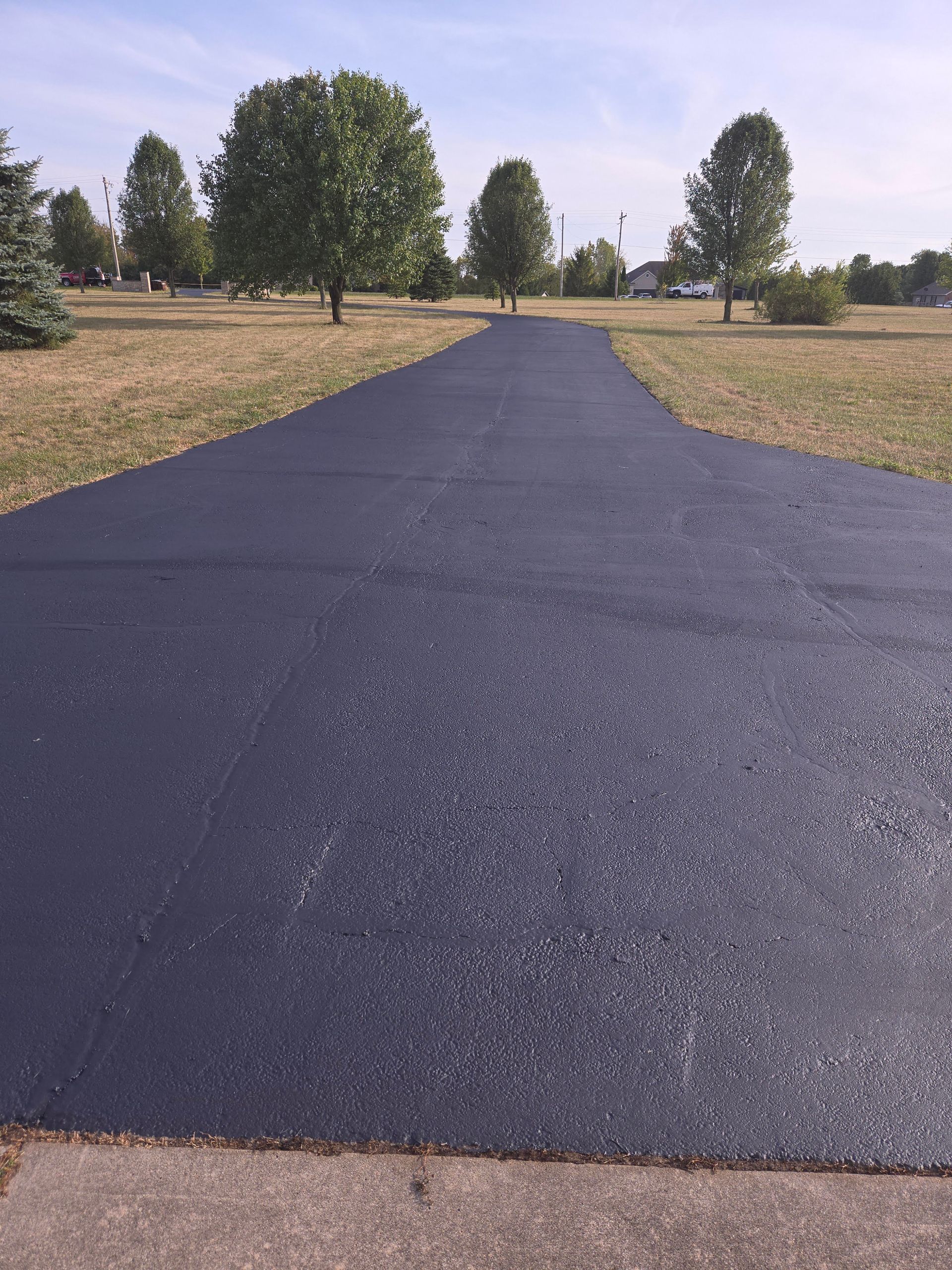 A black asphalt driveway going through a grassy field.