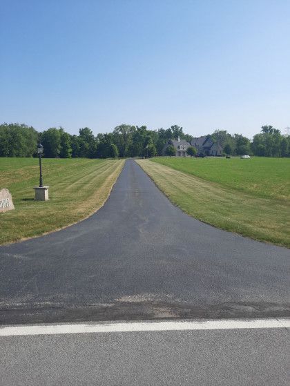 A road going through a grassy field with a house in the background.