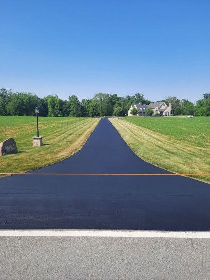 A road going through a grassy field with a house in the background.