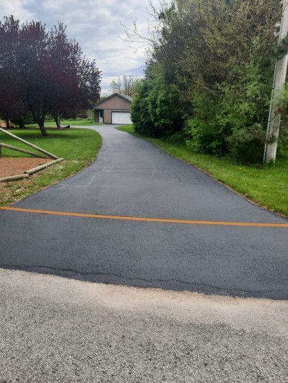 A driveway leading to a house with a garage and trees on both sides.