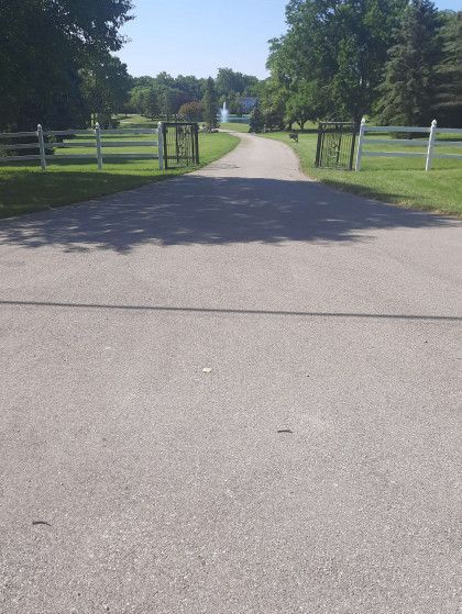 A road with a fence on the side of it leading to a field.