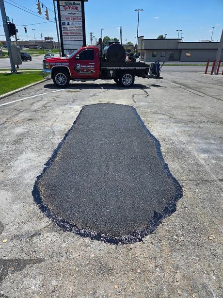 Asphalt patch on a parking lot. A red truck with equipment is parked nearby.