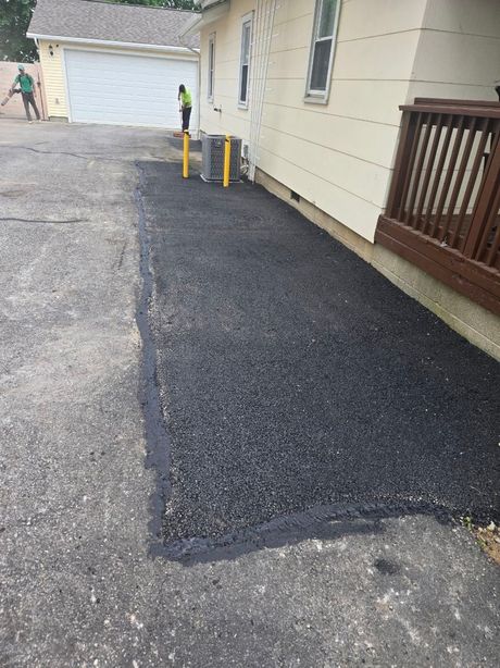 Asphalt patch next to a building and deck. Worker in the background.