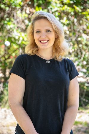 Woman with blonde curly hair, wearing a black shirt, smiling outdoors.