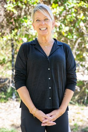 Woman with blonde hair smiles in black shirt outdoors.