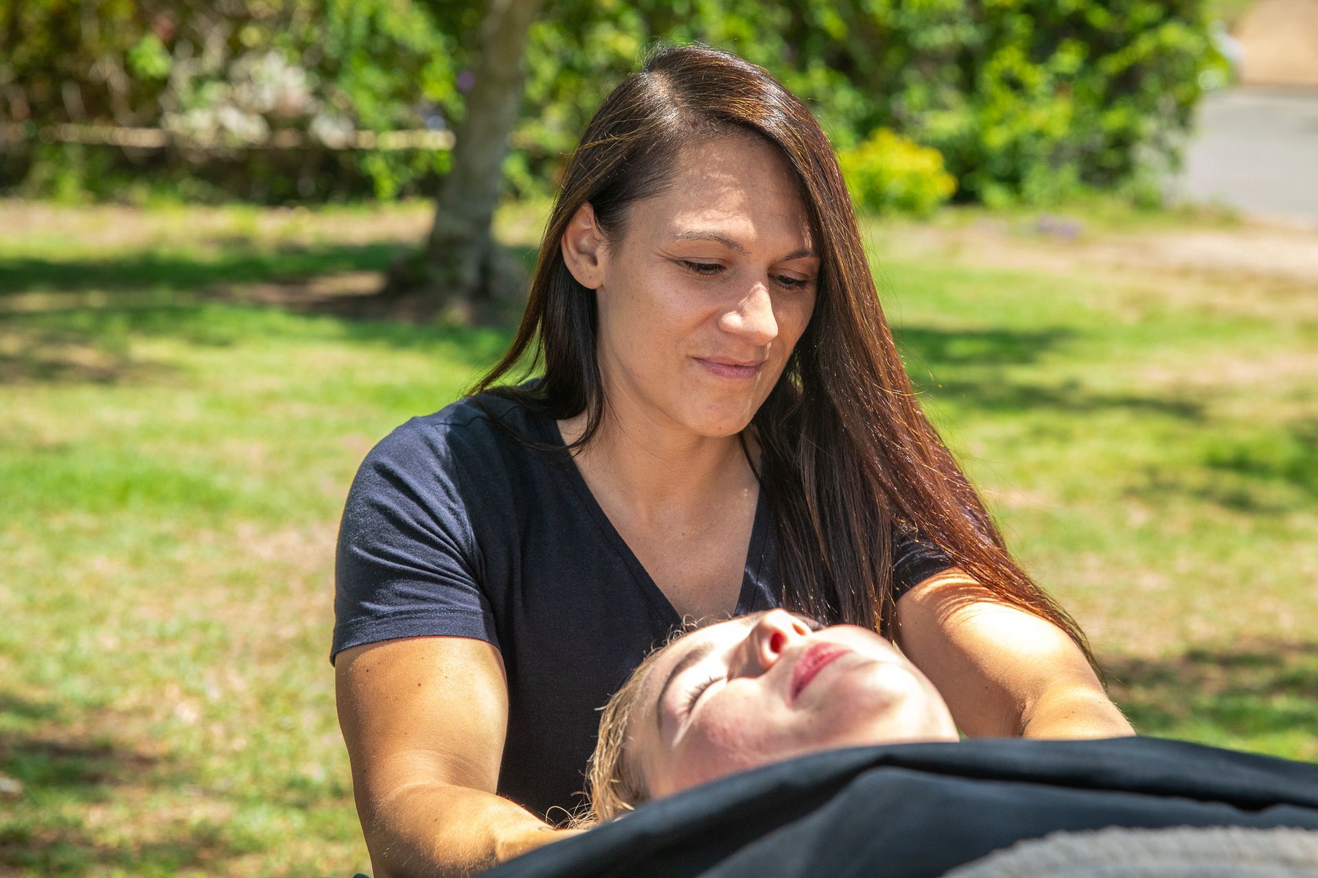 Woman giving massage to another person outdoors.