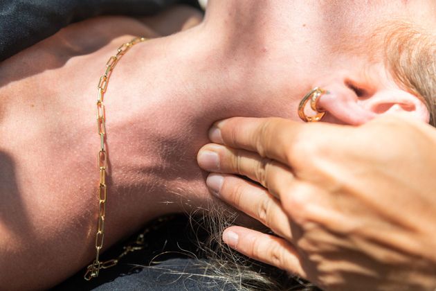 Person's neck and ear with hand touching it; gold chain and hoop earring visible.