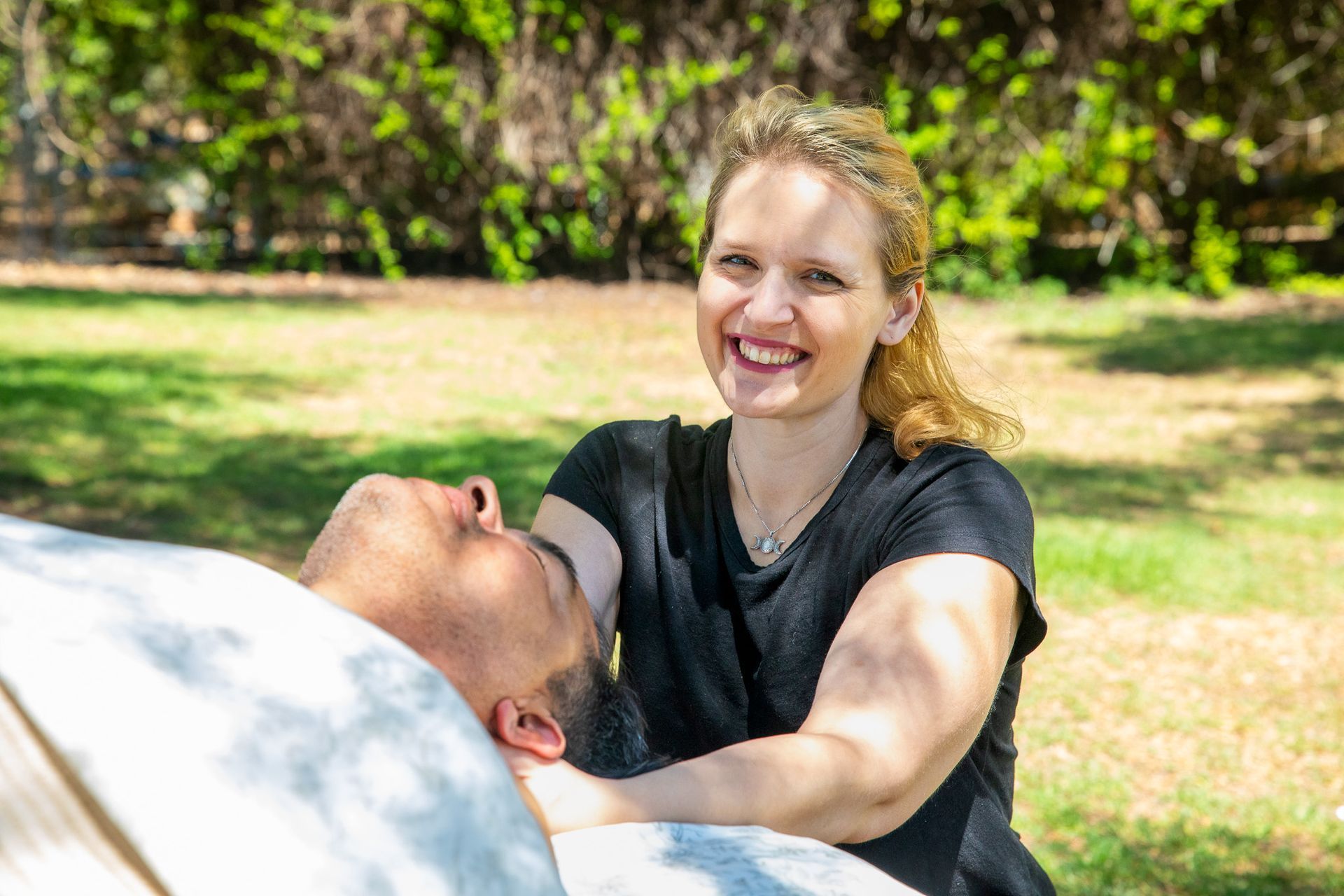 Woman giving face massage to a man outdoors, smiling.
