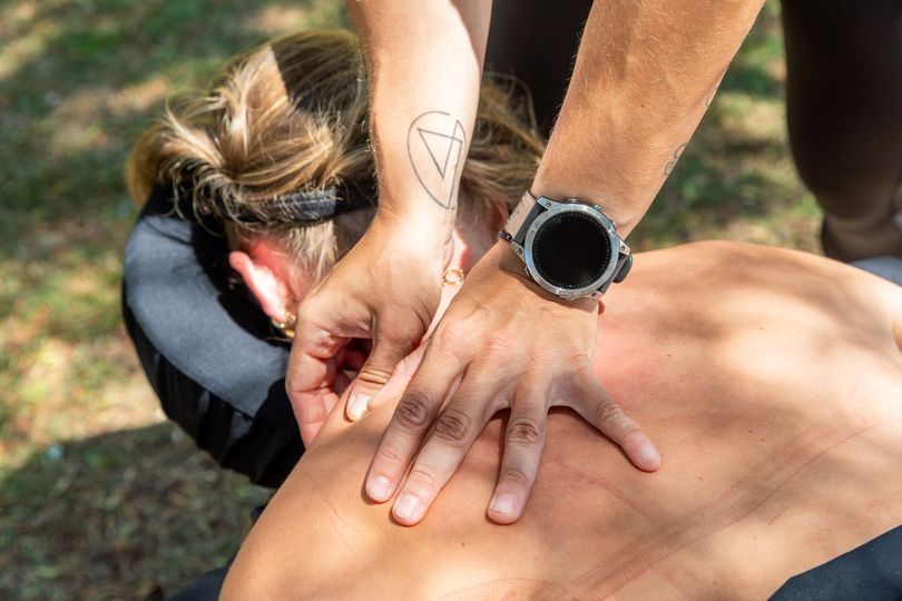 Person receiving massage on back outdoors; arm with tattoo and watch.