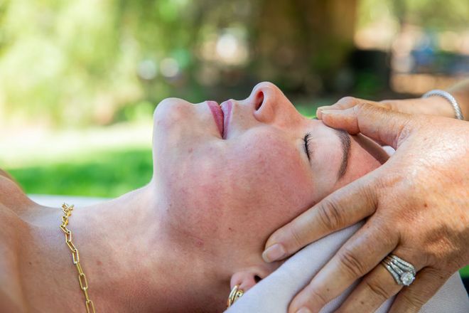 Person receiving a facial, eyes closed, hands holding sponges, in a spa setting.
