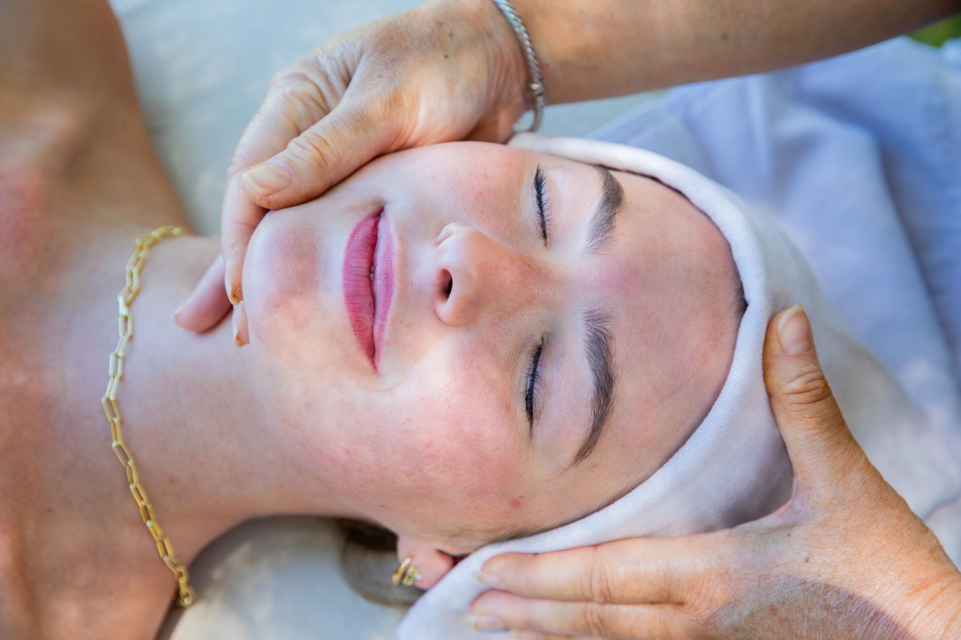 Woman receiving a facial massage, eyes closed, outdoors. Hands on face.