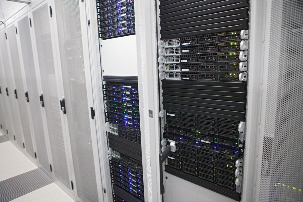 Rijen serverracks in een datacenter. De servers zijn zwart en stralen blauw en groen licht uit.