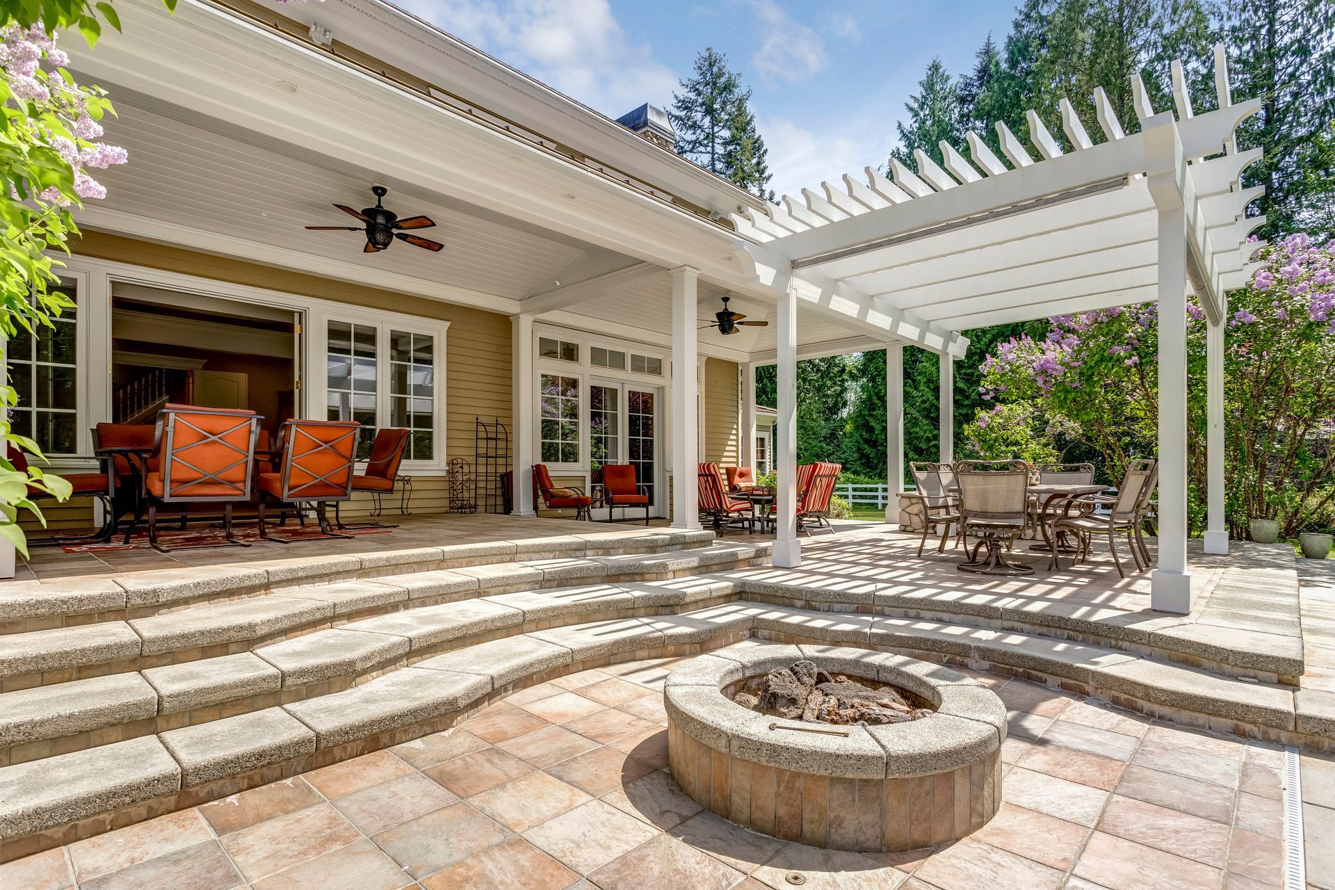 An inviting outdoor deck patio space featuring a white dining pergola, surrounded by lush greenery.