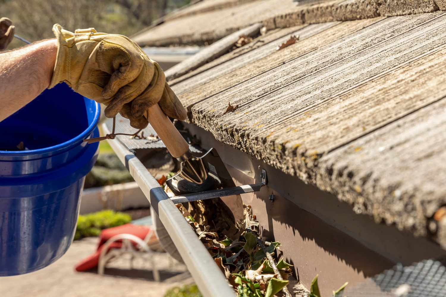 An individual wearing protective gloves and using a long-handled tool to clean debris from gutters, ensuring proper water flow and preventing potential damage.