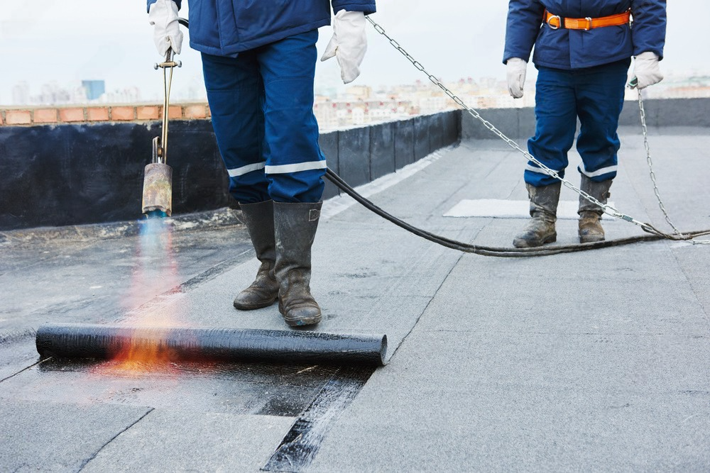 two men are working on a roof with a torch