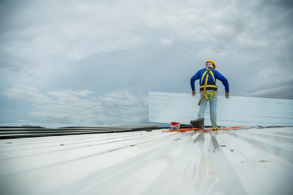 A man is standing on top of a white roof.