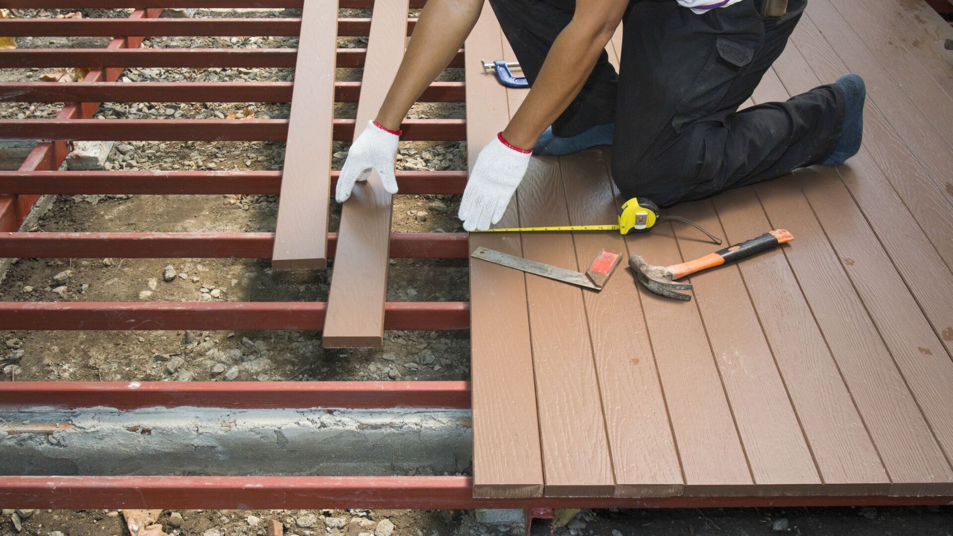 An experienced worker repairs a wooden deck, using a hammer and nails to secure loose boards and ensure stability.