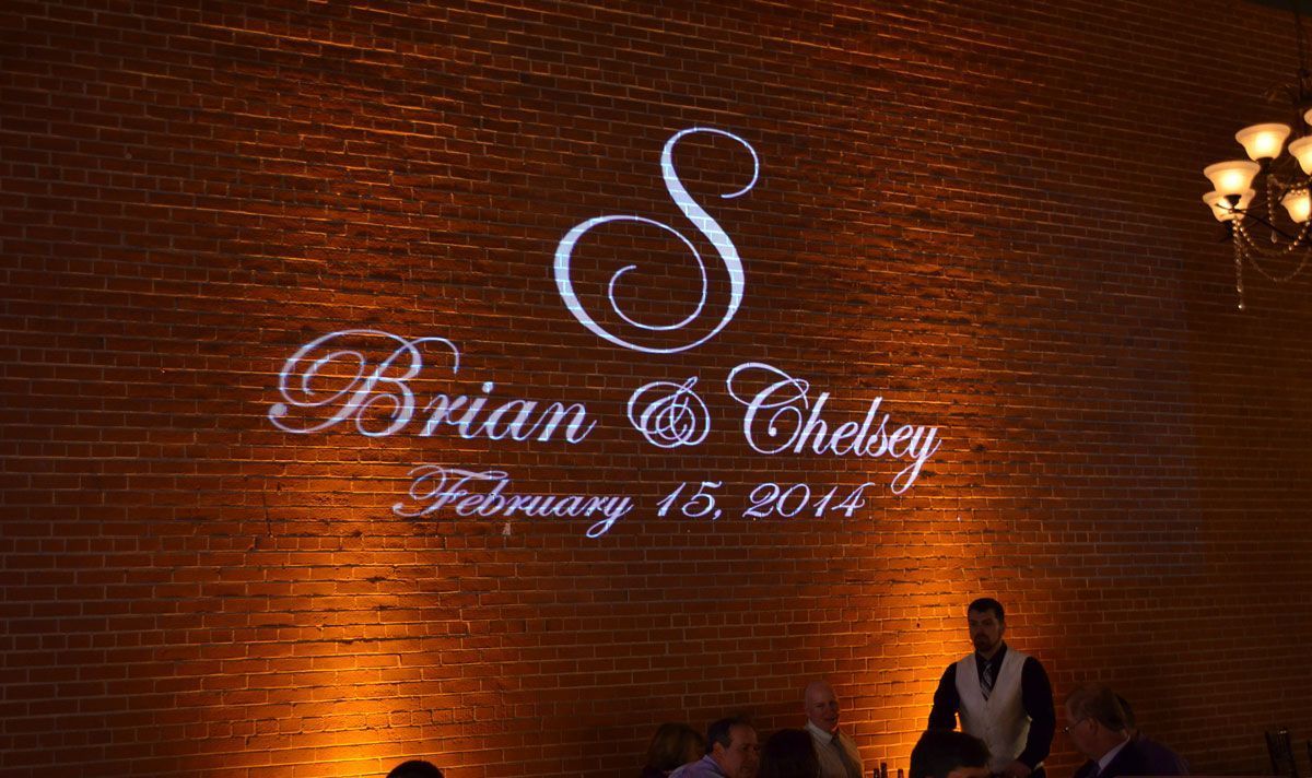 A couple 's wedding logo is projected on a brick wall.