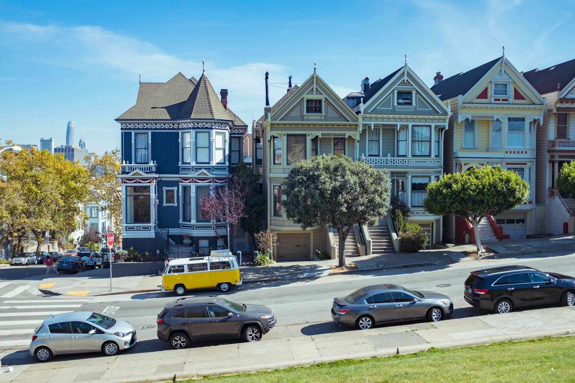 The Painted Ladies in San Francisco with a blue house, historic Victorian homes, a yellow van, and cars on a sunny street.