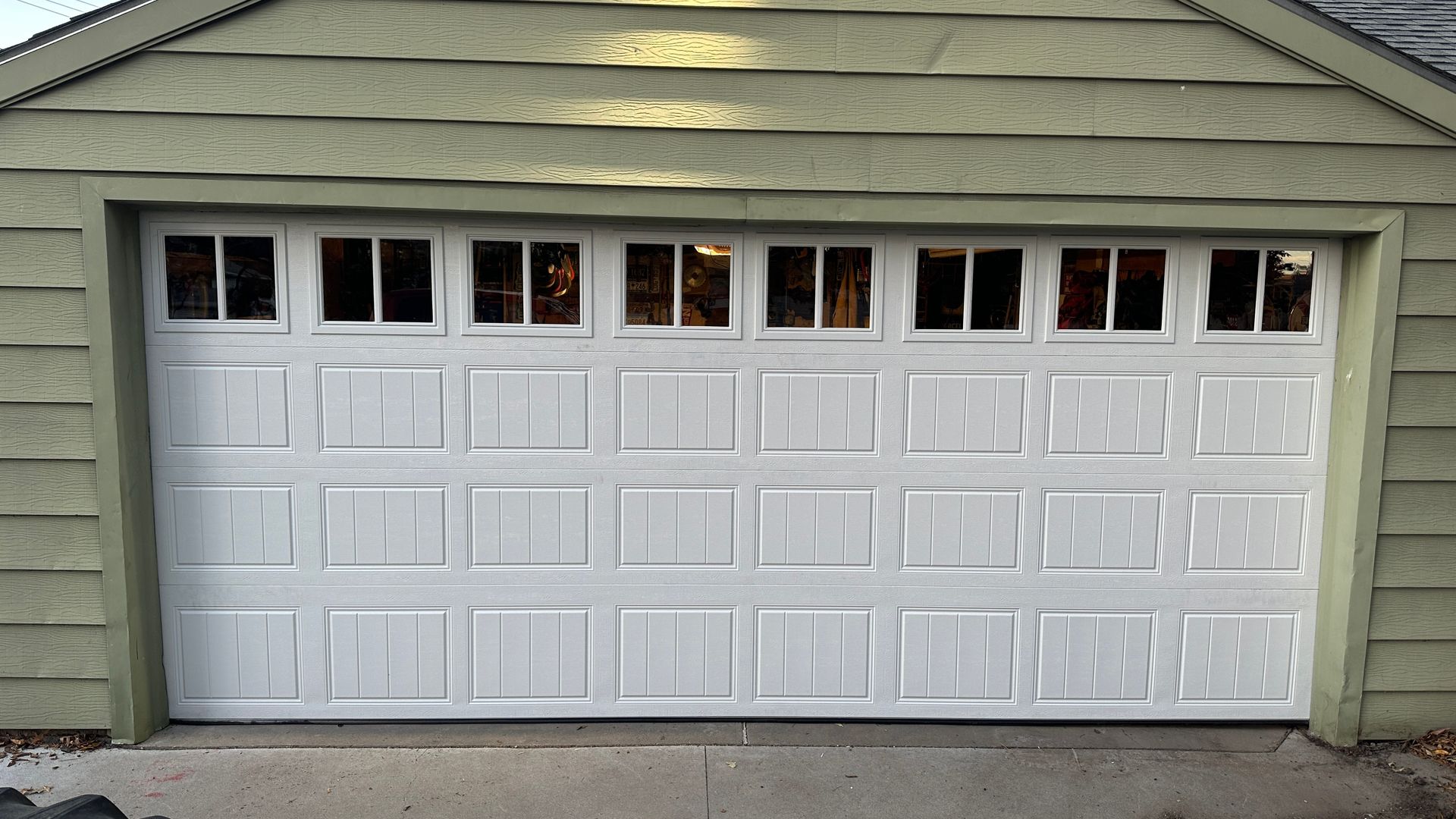 A worker in a red uniform and safety glasses installs a metal garage door panel.