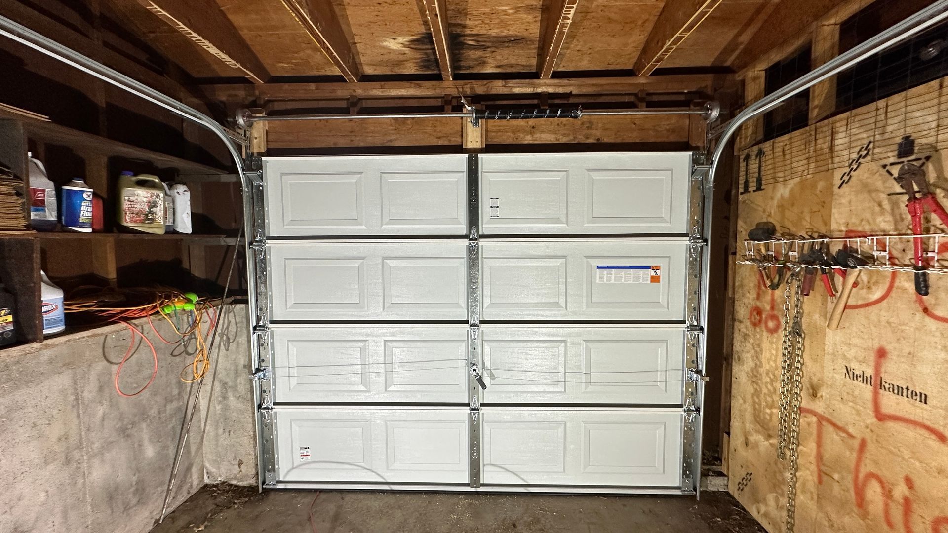 A blue sectional garage door partially open, revealing a view of a green lawn in a clean, modern garage interior.