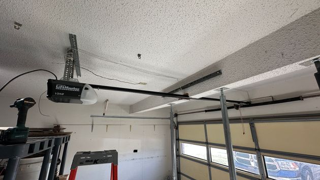 A two-story suburban house with brown vertical siding, stone accents, two white garage doors, and a front entrance.
