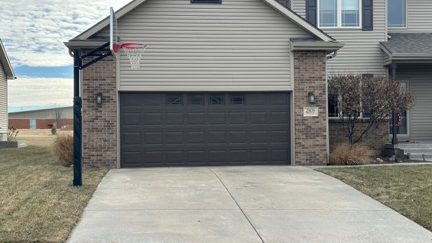 A beige two-car garage with arched windows, decorated with potted pink flowers on a paved driveway in front of a house.
