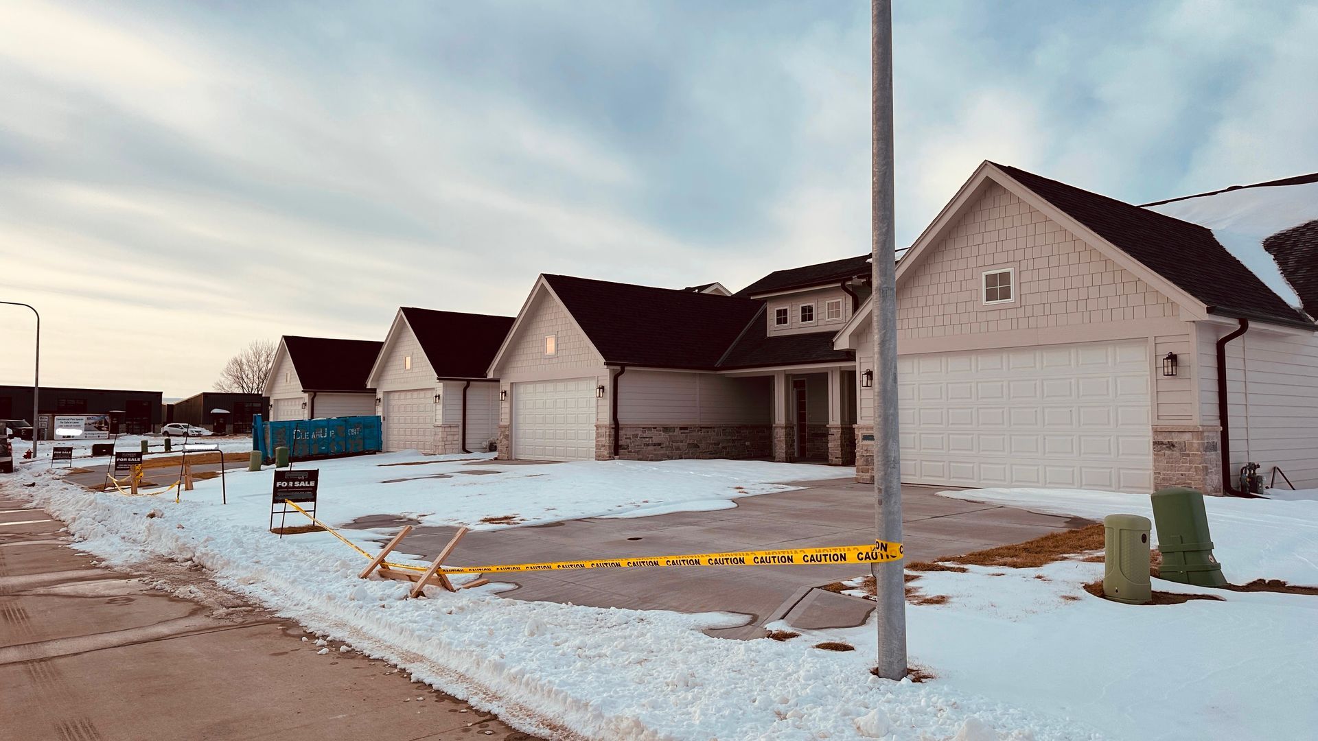 A white car parked in front of a white garage door of a house with a shingled roof and tan exterior.