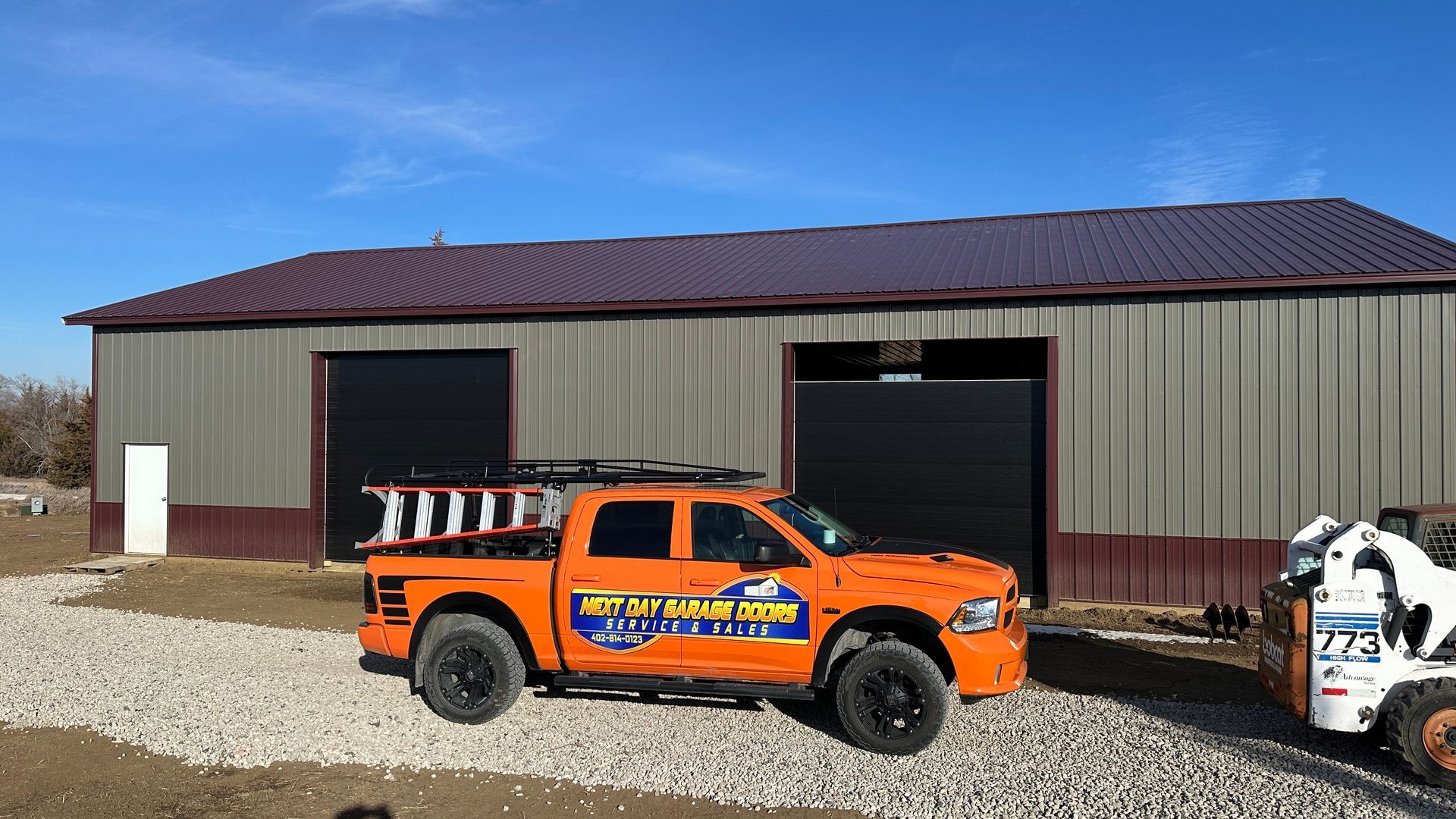 A green garage with a white door and trim, situated on a paved lot with a small patio table set to the side.