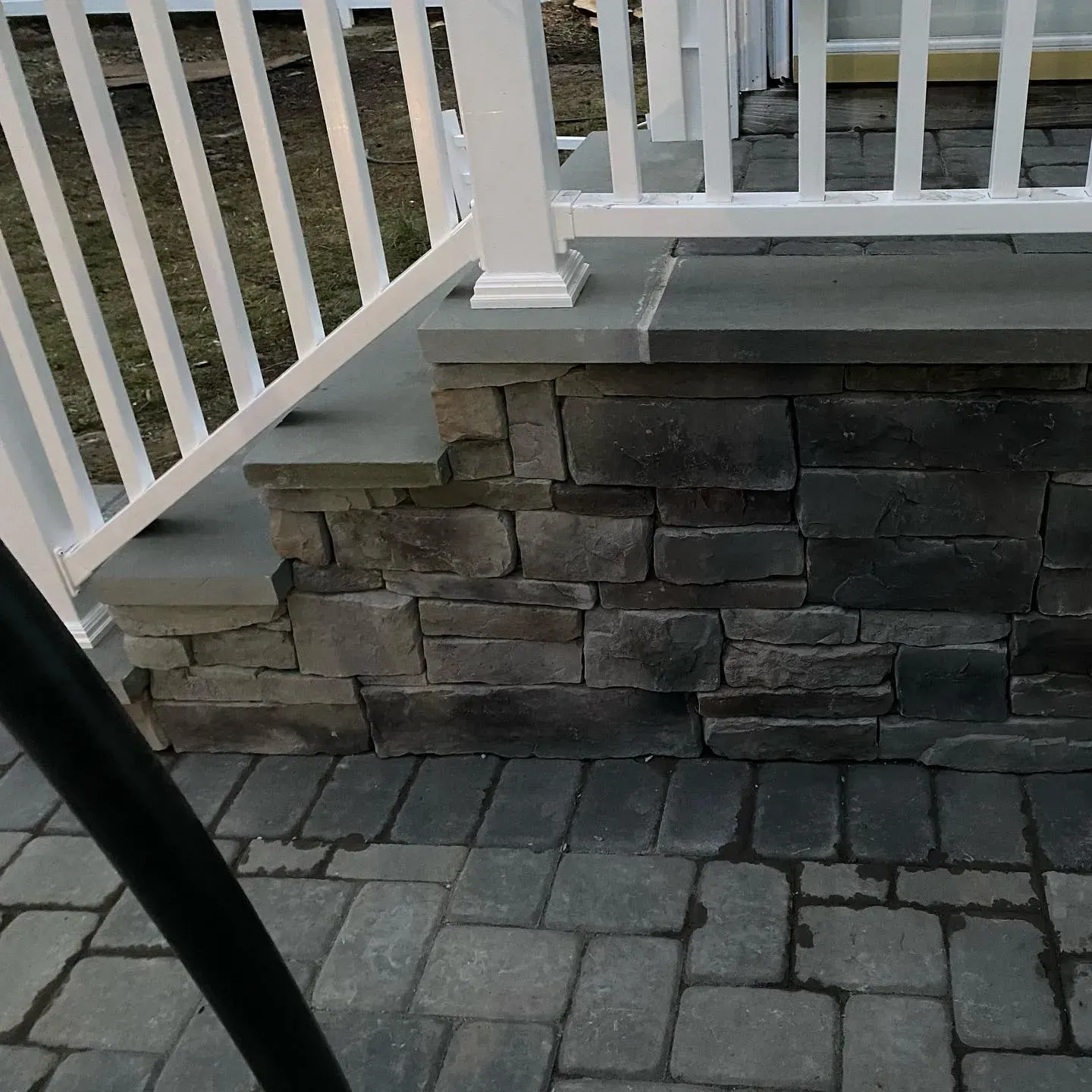 Stone wall with white railing and brick paving.