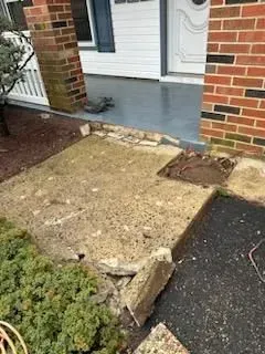 Damaged concrete walkway and porch in front of a house.