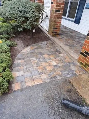 Brick paver walkway leading to a house entrance. The path curves around landscaping.
