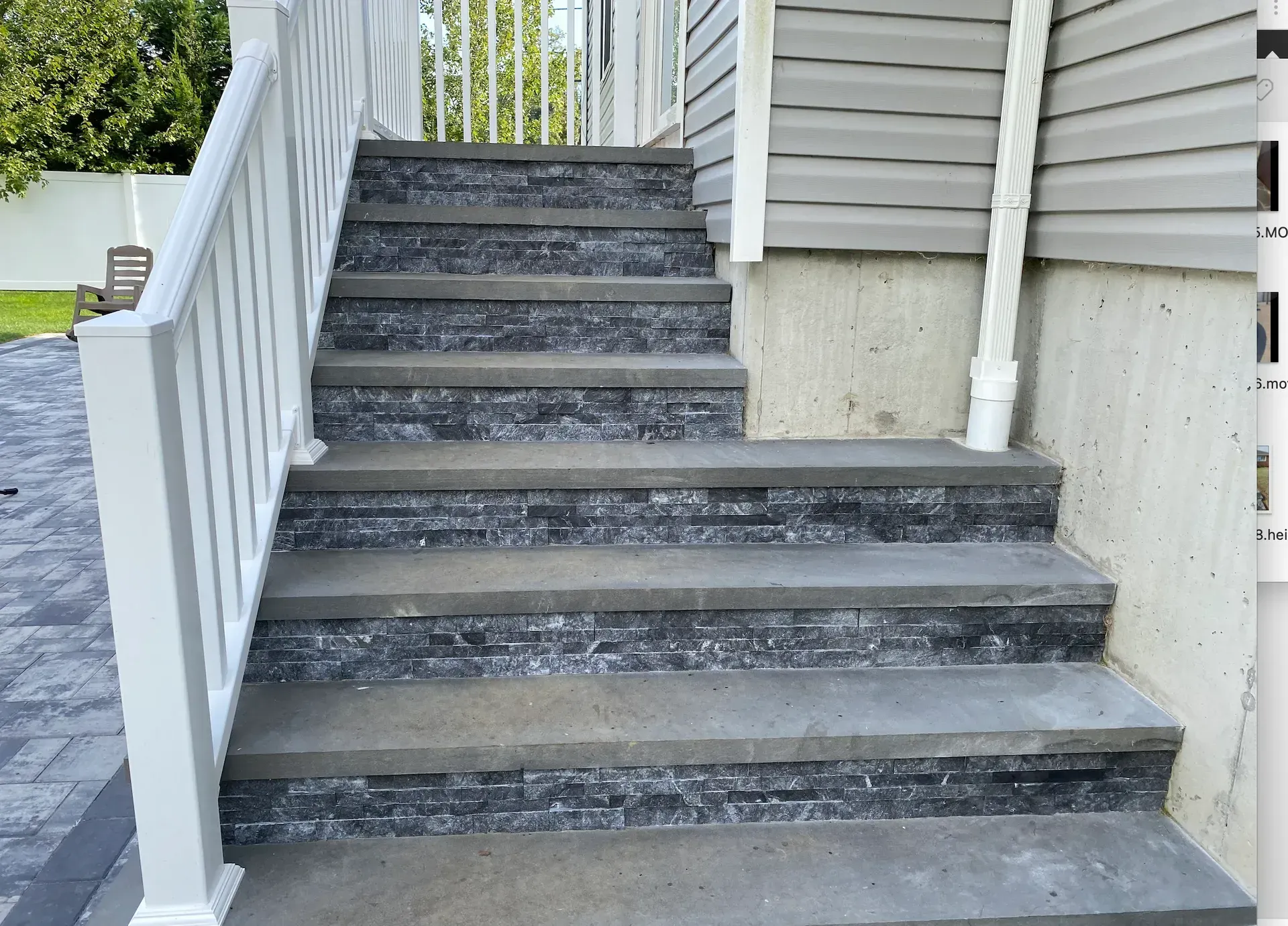 Outdoor concrete stairs with dark stone risers and white railing.