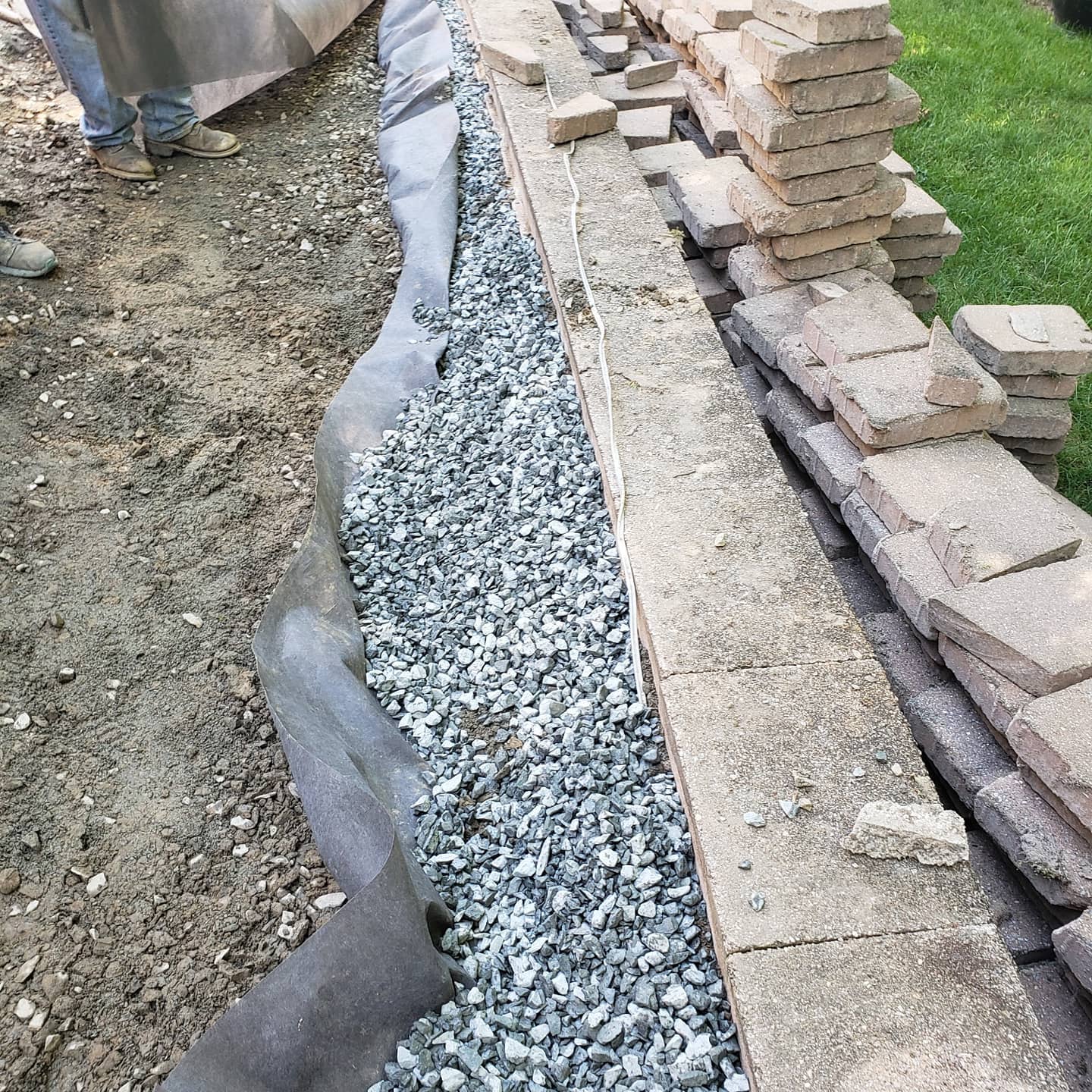 Construction of a retaining wall: gravel, fabric lining, cement blocks, and stacked bricks.