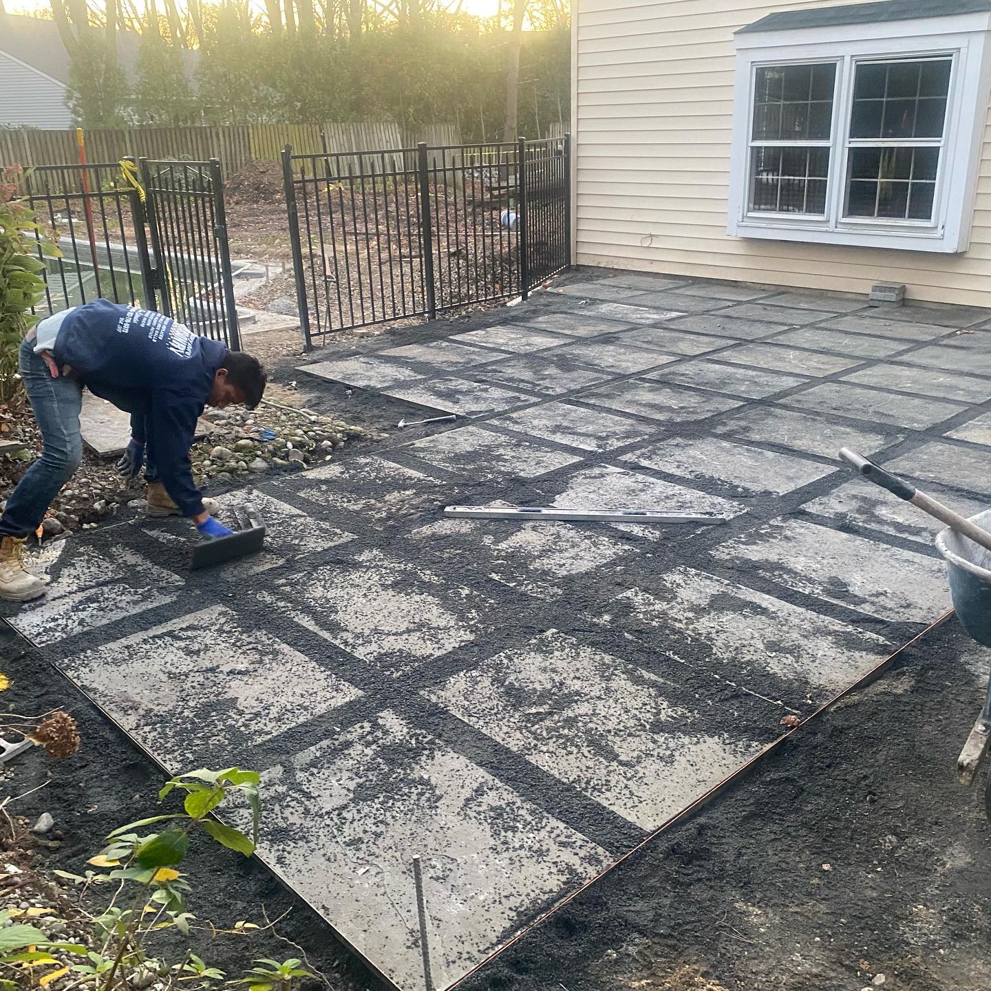 A person spreading gravel between concrete patio tiles next to a building.