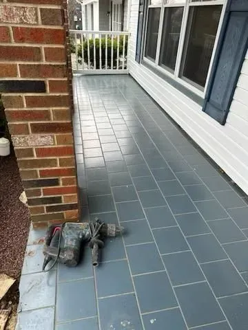 Porch with gray tiled floor, brick pillar, white siding, and a jackhammer.