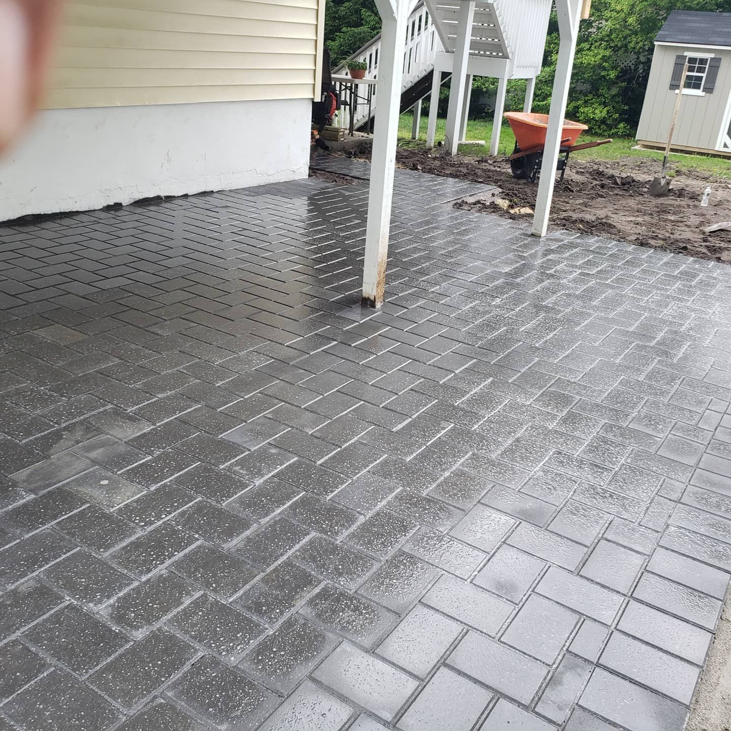 Brick patio with wet, gray pavers under a deck and near a house.