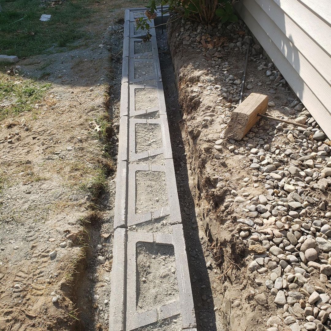 A narrow concrete wall with open rectangular spaces sits between a gravel area and dirt.