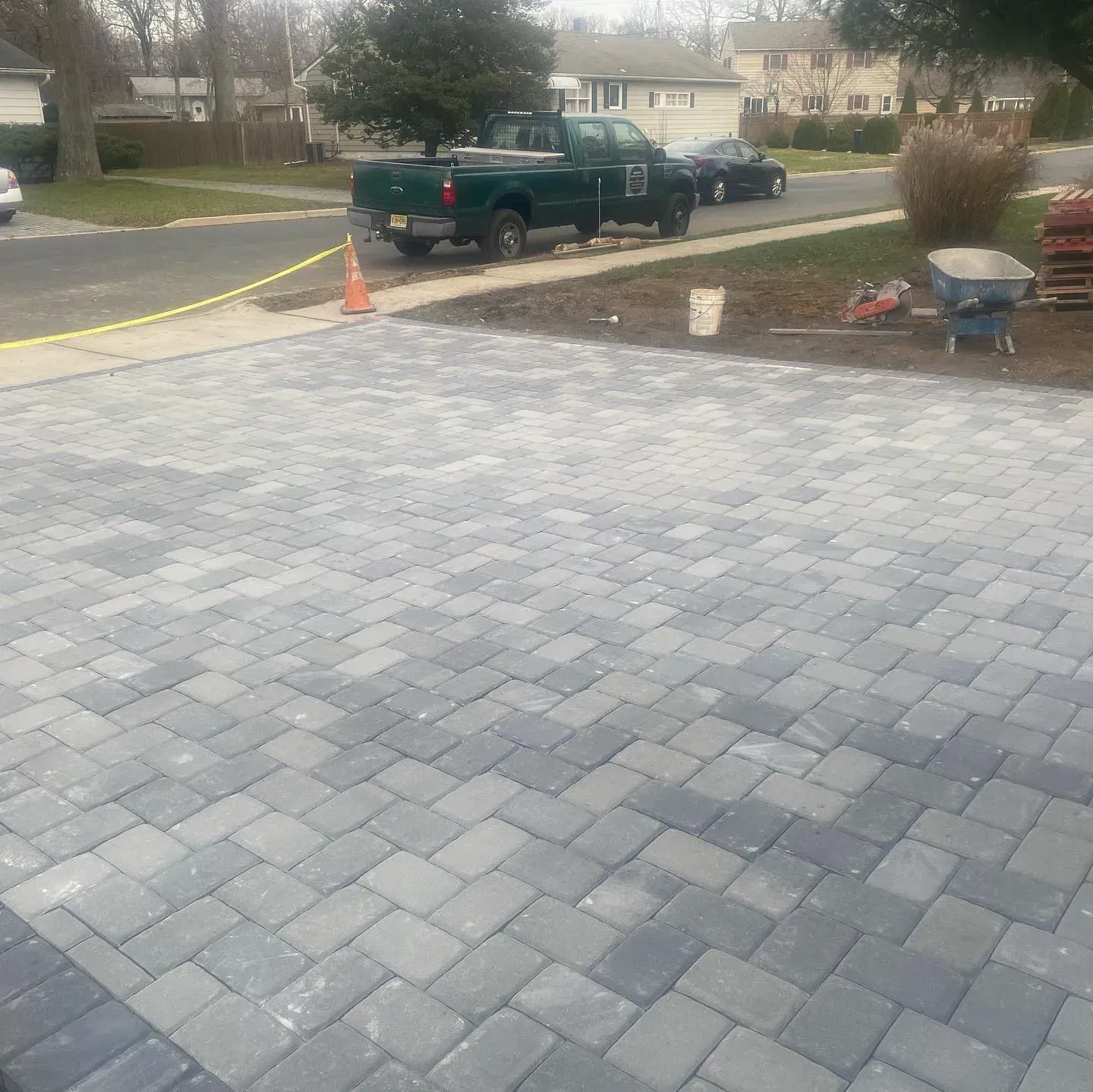 Driveway paved with grey and blue interlocking bricks; truck and car in background.