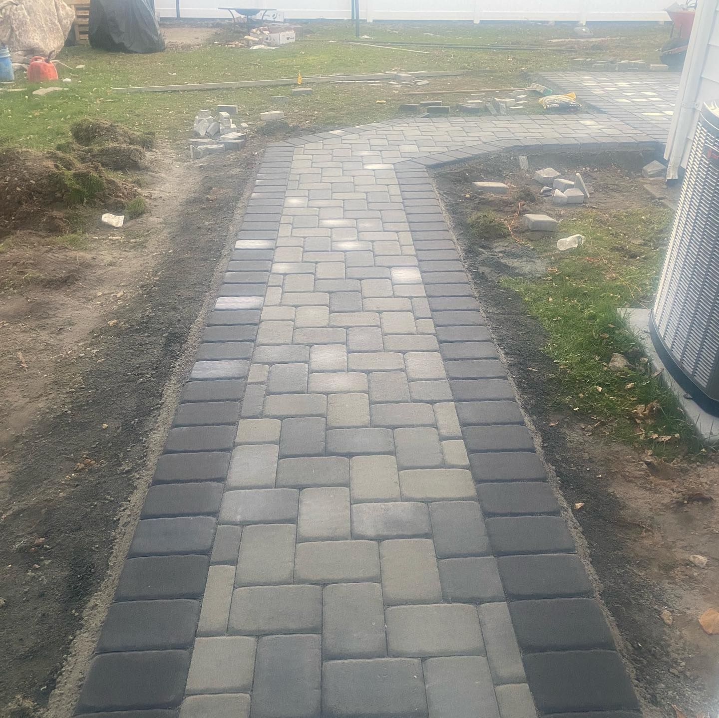 Brick pathway with gray and black pavers leading through a yard.