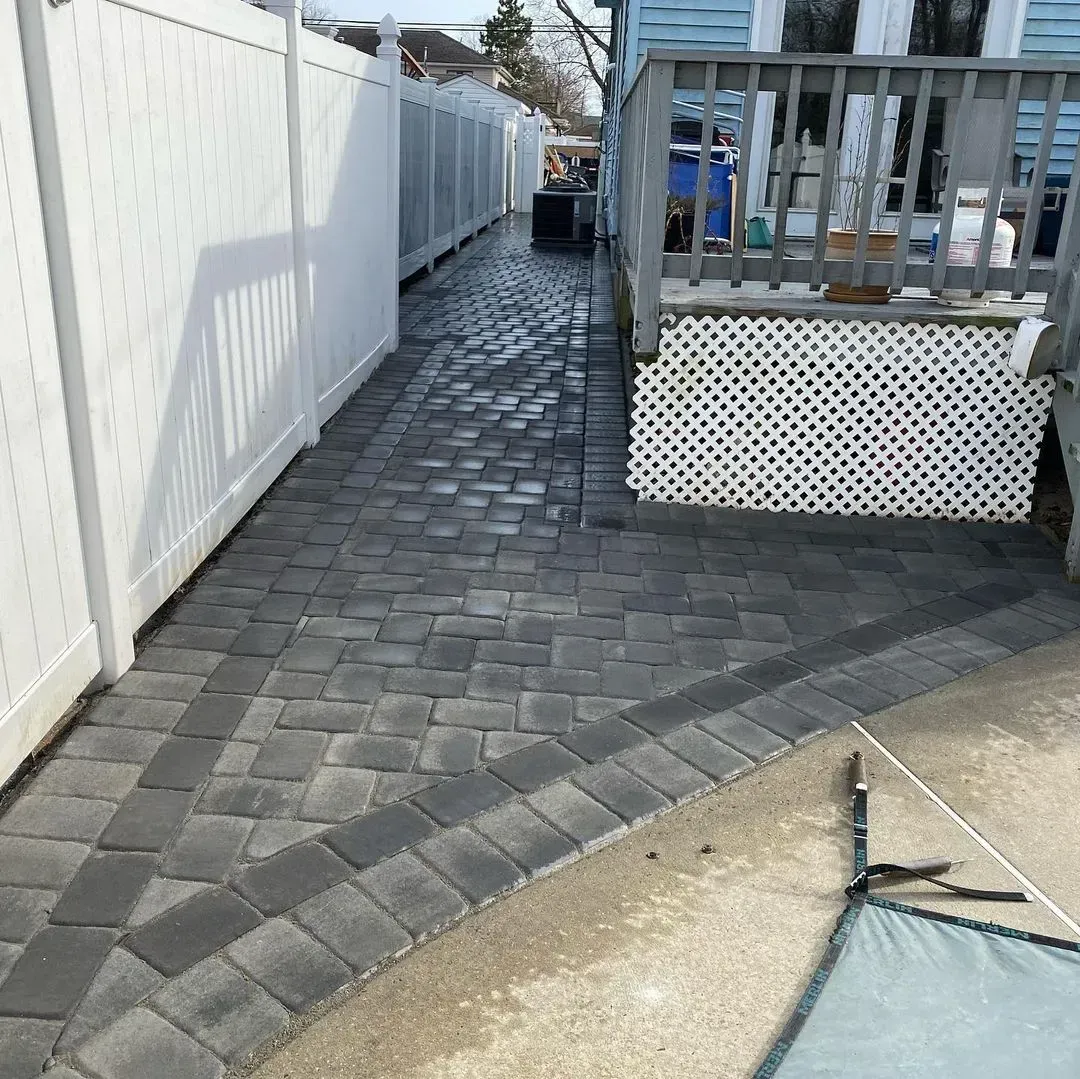 Brick pathway next to white fence and a house deck.