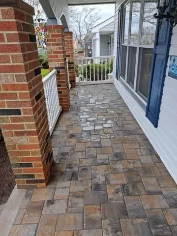 Brick and paver porch with white railing, columns, and blue shutter.