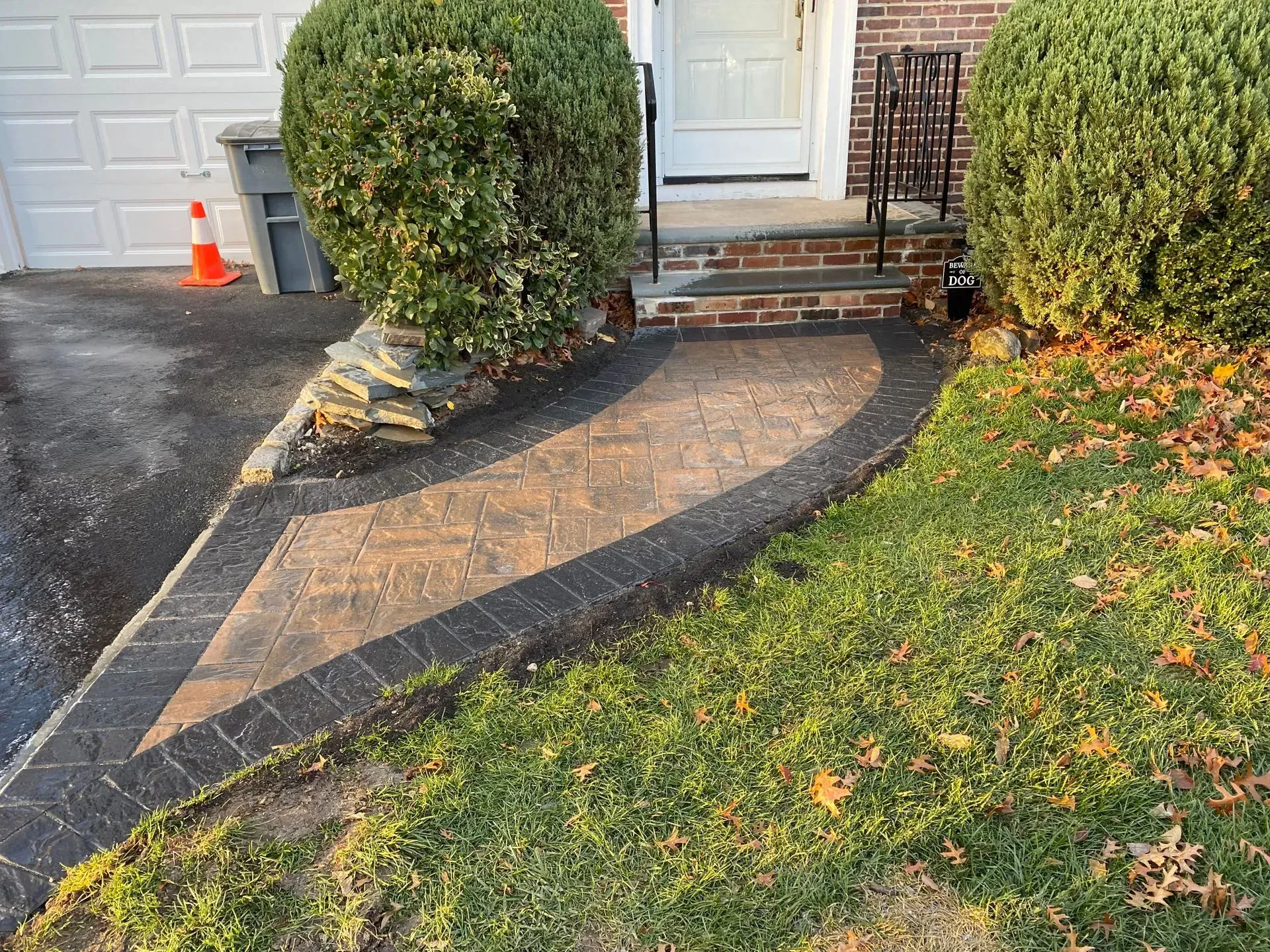 A curved paved walkway leading to brick steps and a white door, flanked by green bushes and grass.