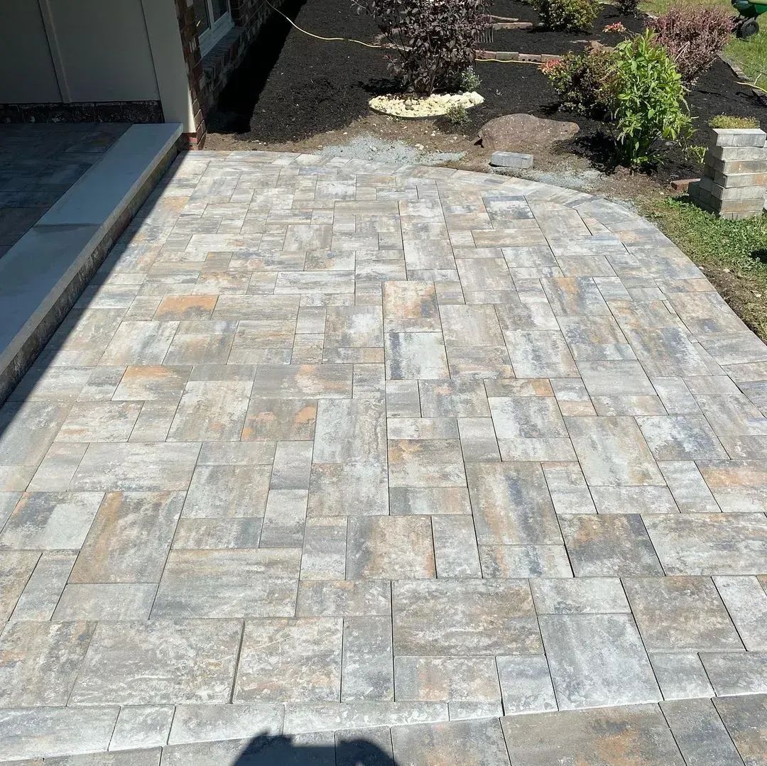 Paver walkway in shades of gray and tan, leading from garage to garden beds with mulch and greenery.