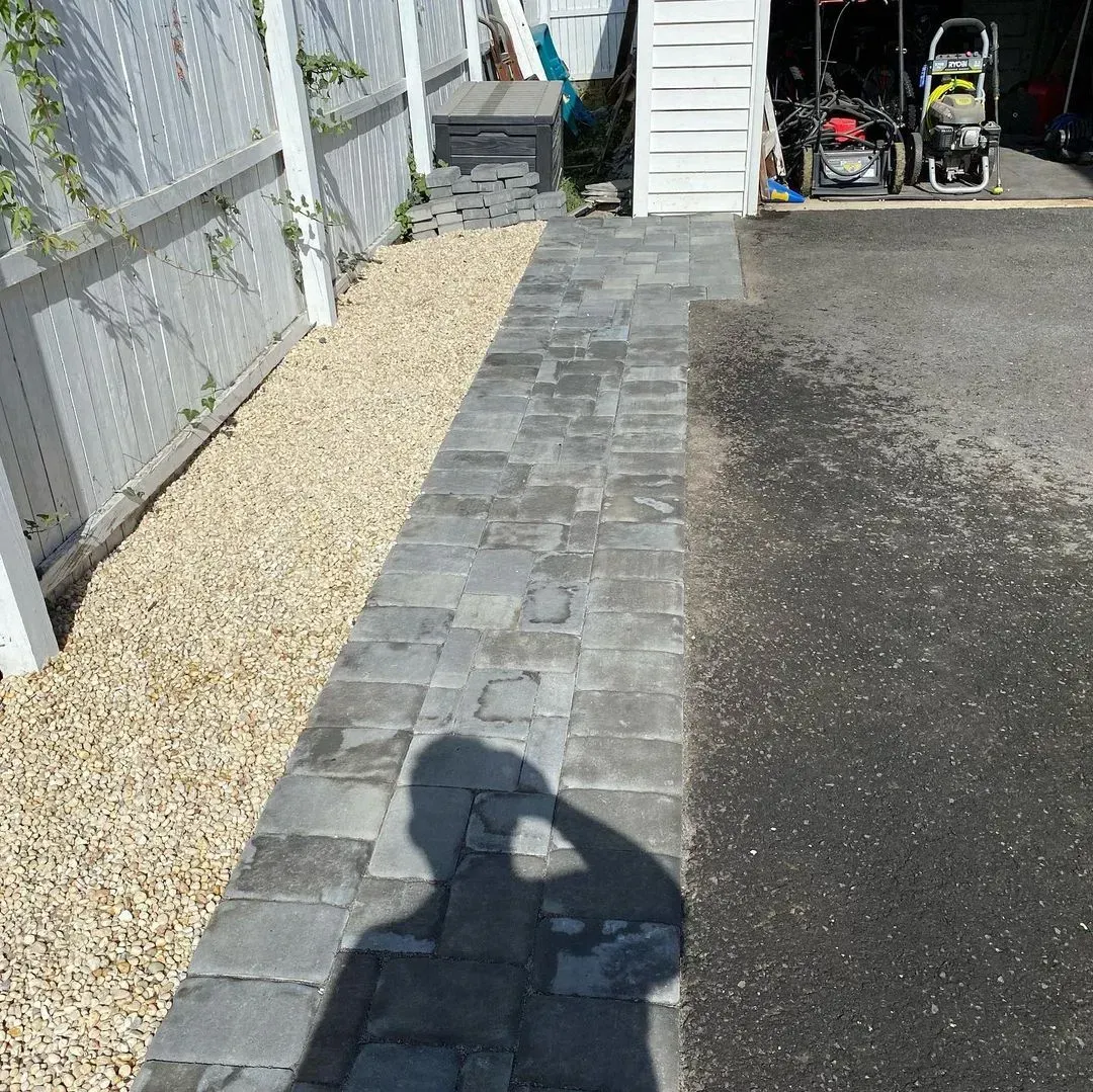 Pathway of gray pavers beside gravel and a fence, leading to a garage entrance.