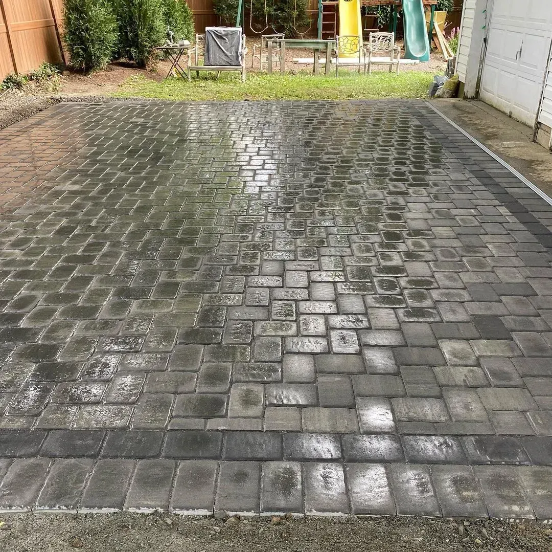 Wet, paved driveway with a garden and play set in the background.