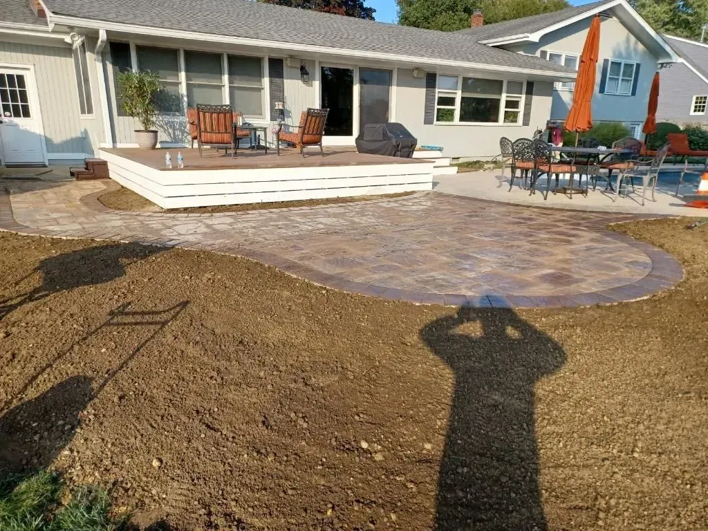 Backyard with deck, patio, and lawn. Shadow of person taking photo visible in the foreground.