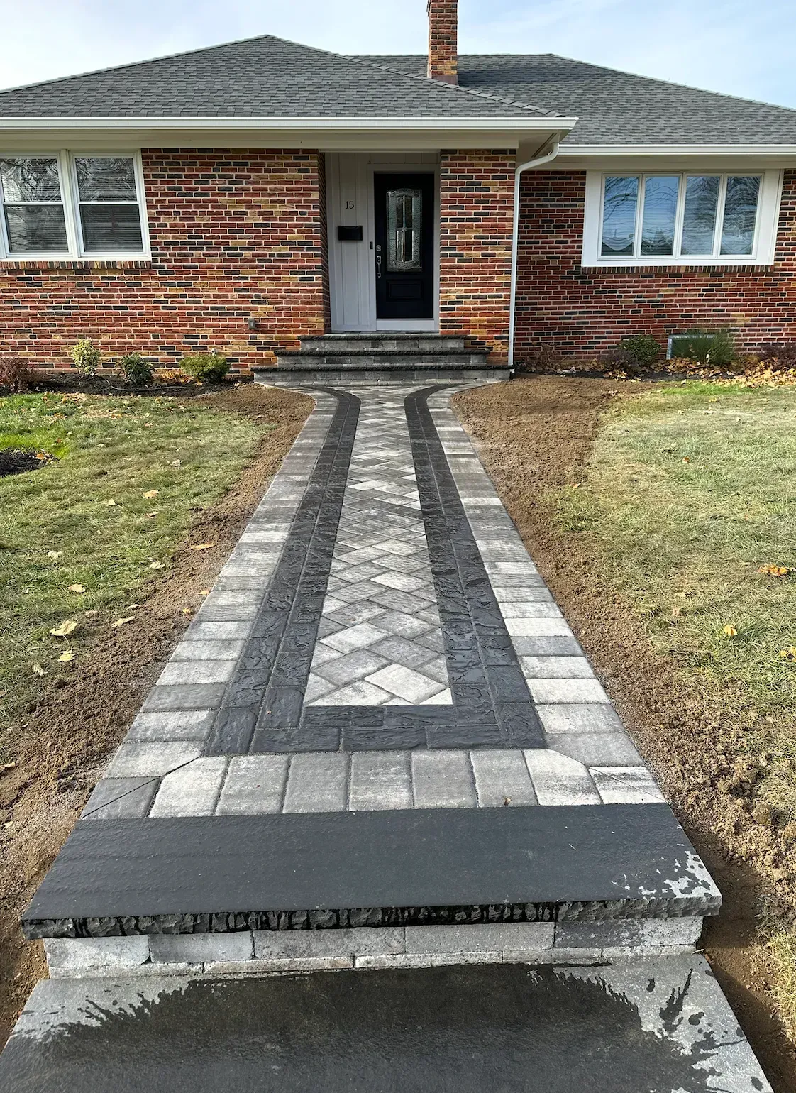 Brick house with new paved walkway leading to the front door. Grey and black paving stones.